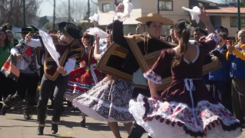 Varias parejas de cueca de frente, acercándose con las faldas en movimiento y los pañuelos en alto.
