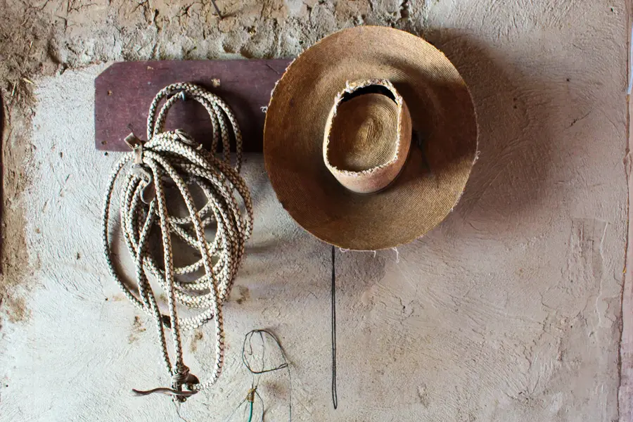 Lazo trenzado y chupalla colgados de una percha de madera en una pared de adobe.