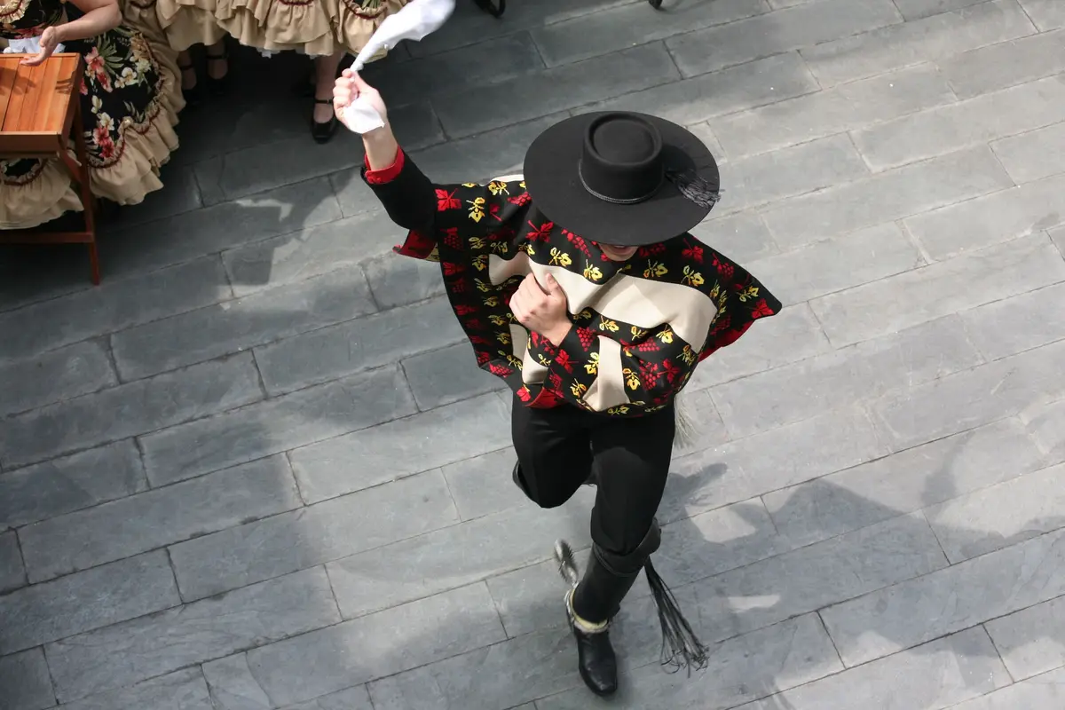 Bailarín de cueca visto desde arriba zapateando: chupalla negra, manta, espuelas y el pañuelo girando sobre la cabeza.